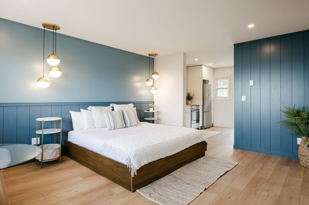 bright hotel room with blue walls and a king sized bed with white bedding. in the background there's a kitchenette