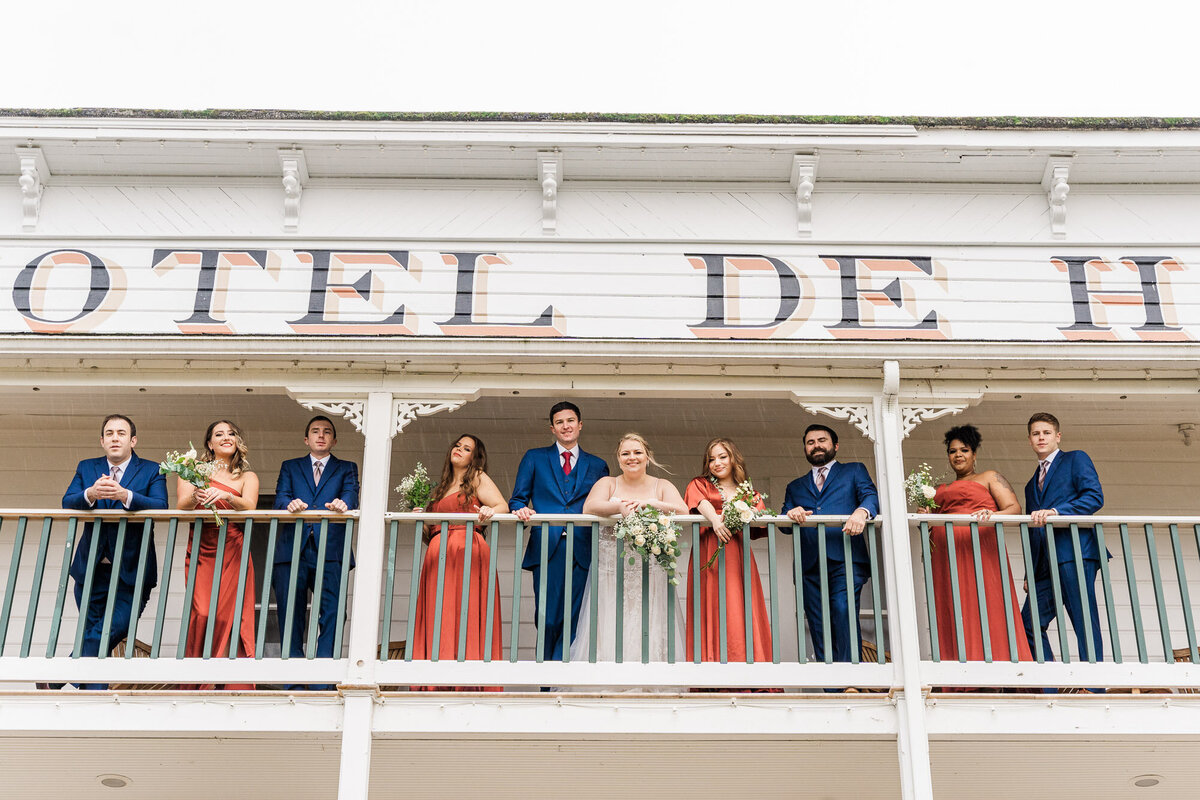 Wedding-party-on-balcony-at-Roche-Harbor-wedding-venue-on-San-Juan-Island-Bridesmaids-in-orange-and-groomsmen-in-blue-photo-by-Joanna-Monger-Photography