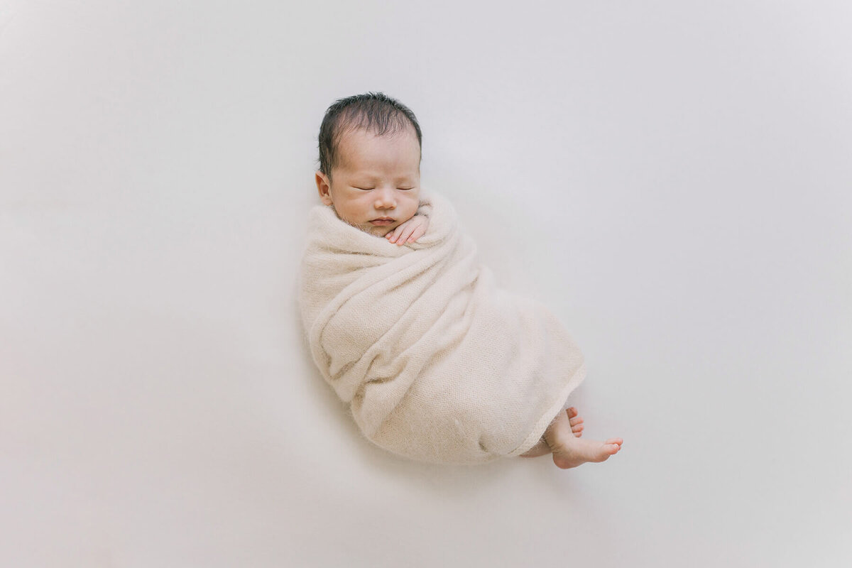 Baby lightly wrapped in angora wraps and sleeping with his hands and feet out. Taken by newborn photographer Yukika Ishikawa Photography.