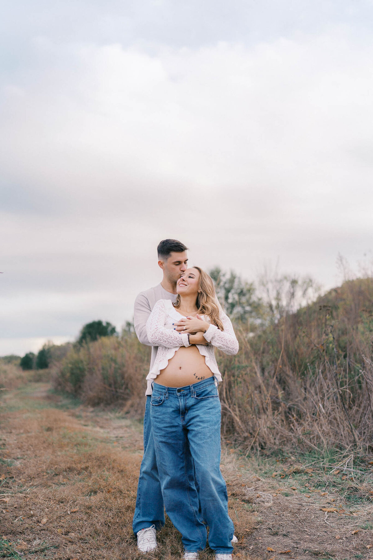 husband holds pregnant wife in field outside in knoxville tennessee during maternity session