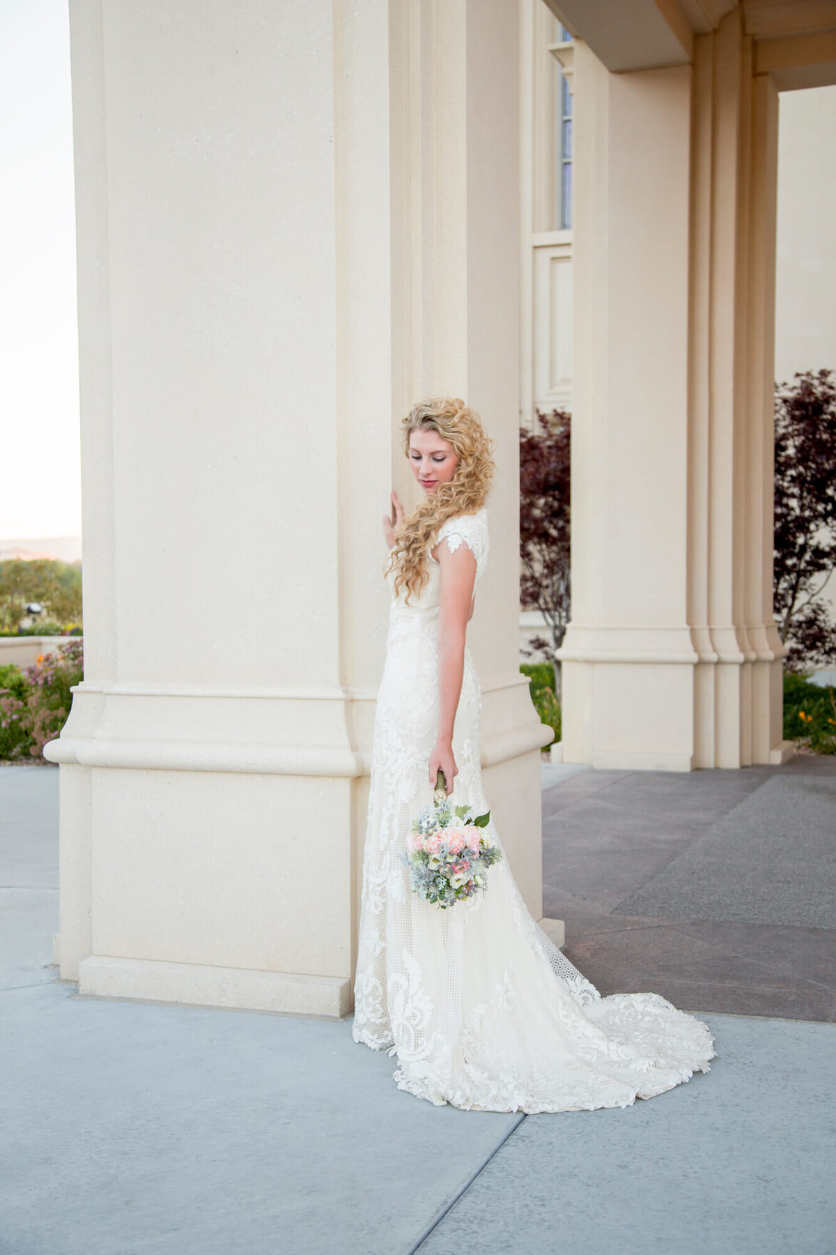 a beautiful curly haired bride looking down at her bouquet by a softly lit column