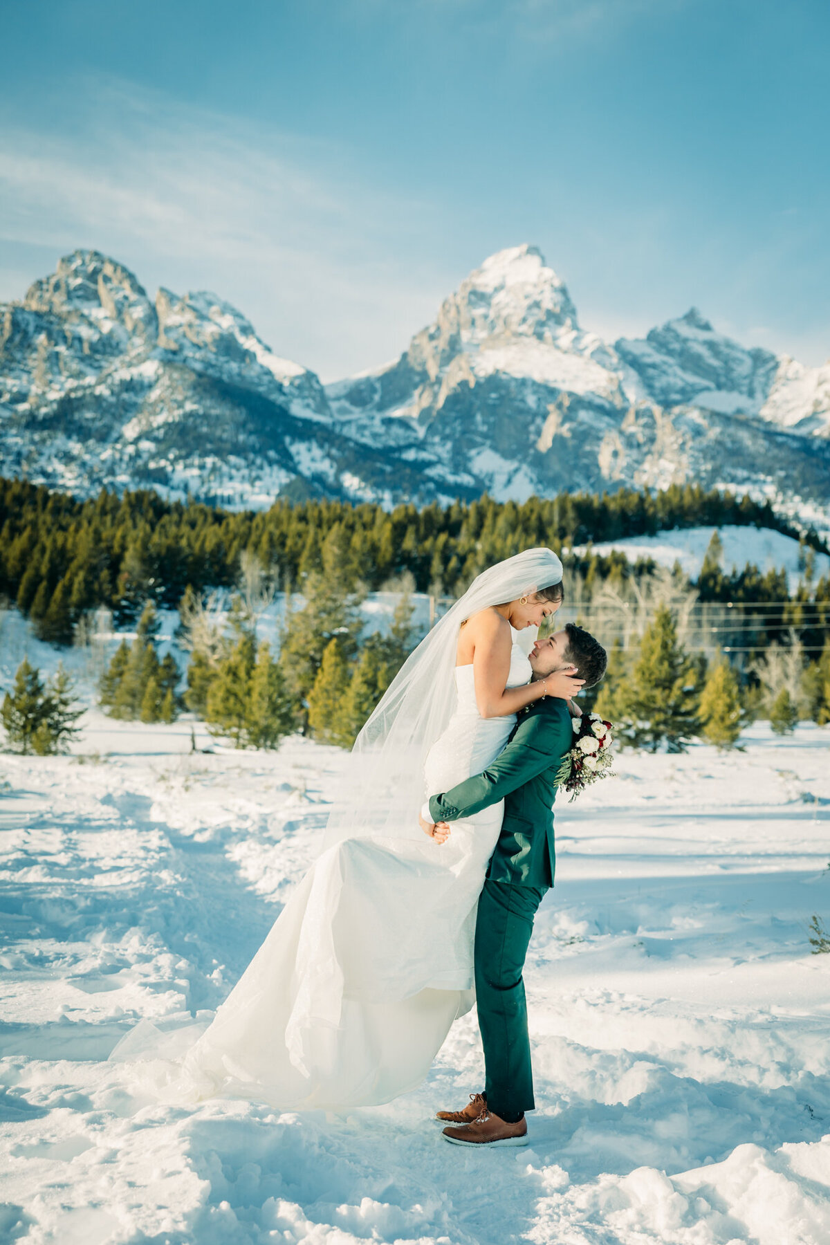 Winter wedding in Jackson Hole Wyoming in front of Taggart Lake Trailhead with bride being lifted by groom in snow romantic classy