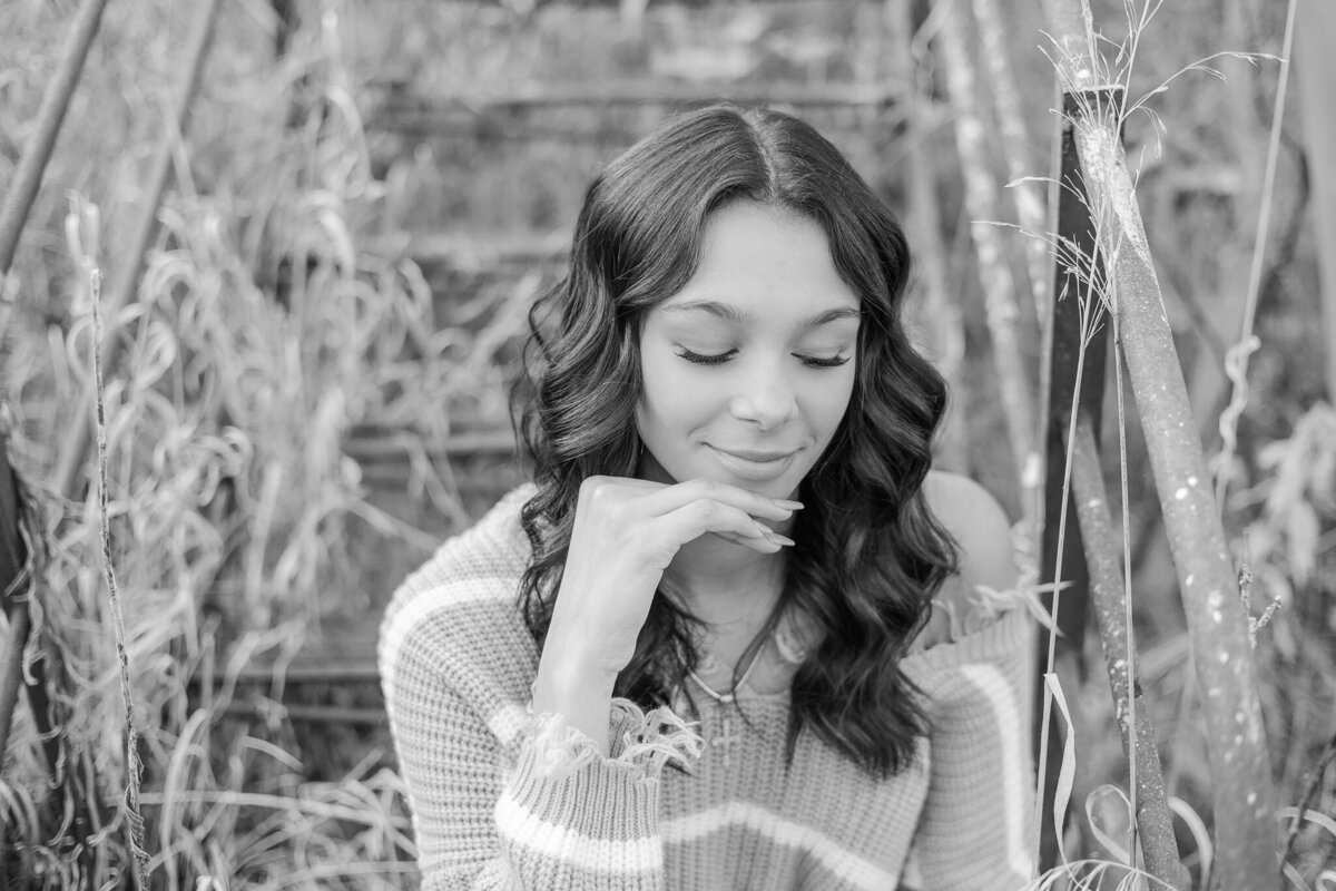 black and white photo of a high school senior female, with long dark hair, hand under chin, looking down smiling softly