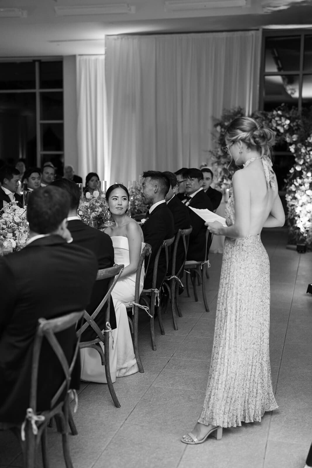 Black and white image of a woman giving a Maid of Honor toast at her sister's wedding.