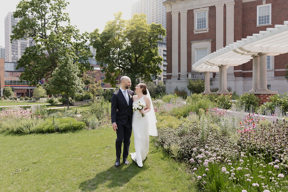 couple walks along Chicago History Museum garden with their arms around each other and they look at each other and laugh