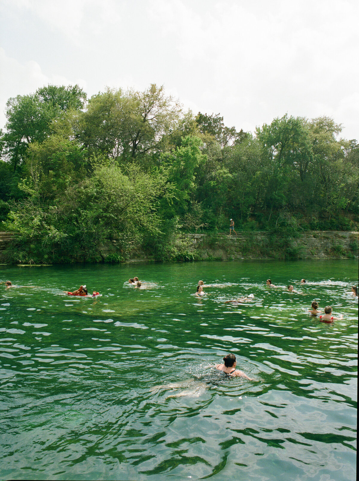 A person swimming in a sunlit lake on a beautiful day, surrounded by nature, captured on film in a candid, unposed moment — by Kate Winters Photography, Carmel wedding photographer.