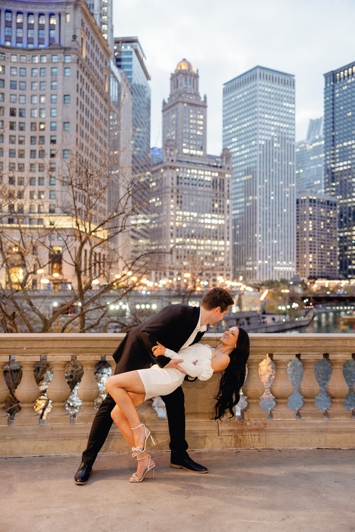 A couple embraces at dusk along Michigan Avenue and the Chicago River, with the city lights creating a romantic and timeless backdrop.