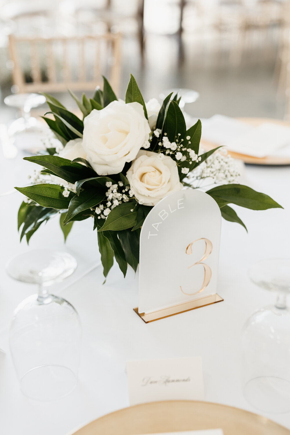 Elegant table centerpiece featuring a stunning arrangement of white flowers in a gold vase with gold acrylic table numbers at Ashford Acres Inn in Cynthiana, KY.