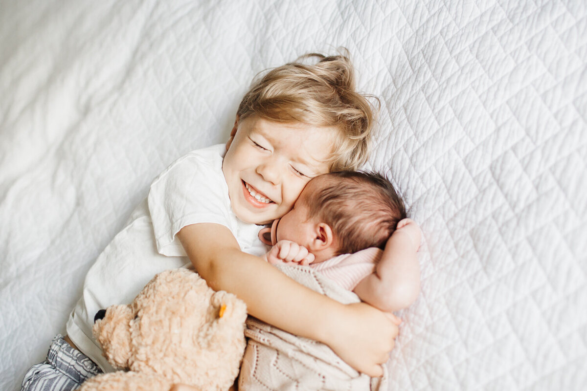 big brother hugging newborn sister on bed