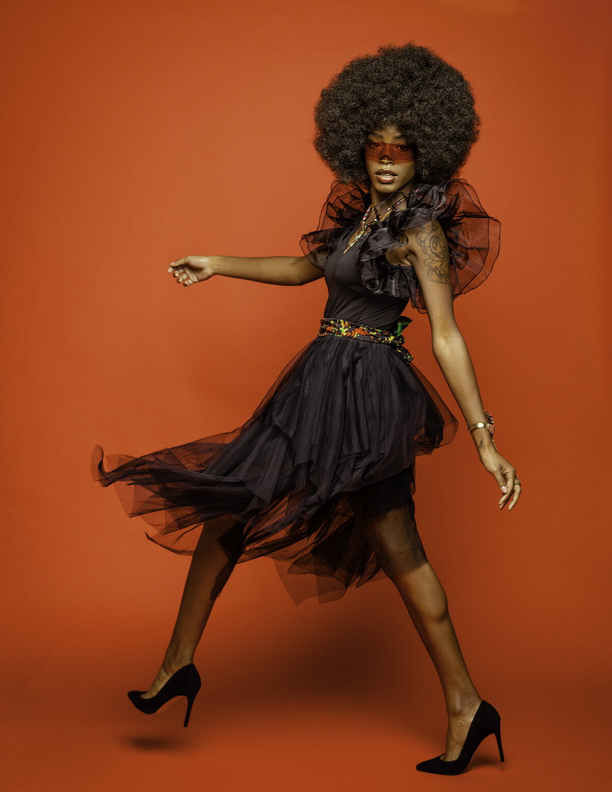 Black woman with afro in black outfit with red glasses