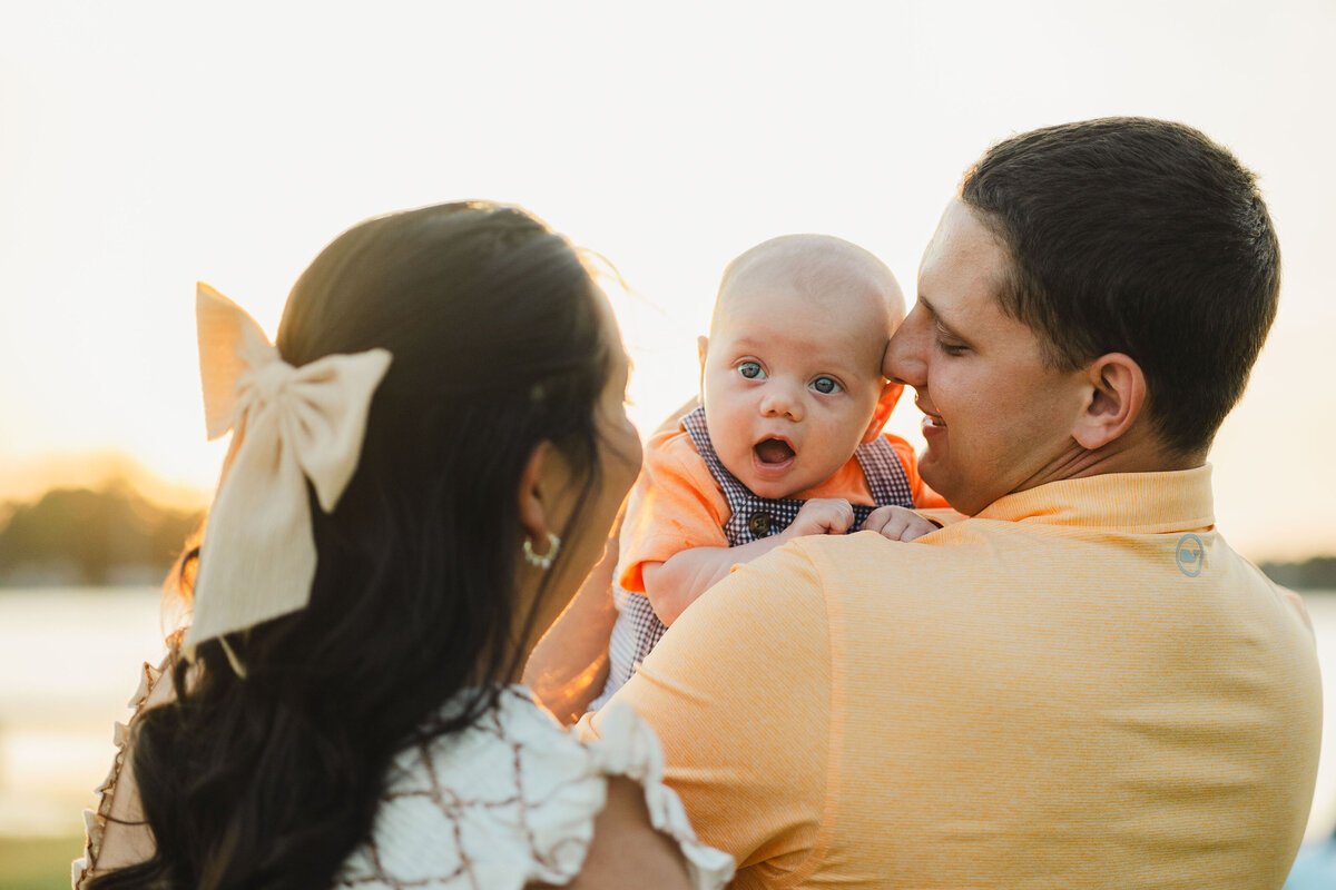 Two parents hold their newborn who makes an excited face.