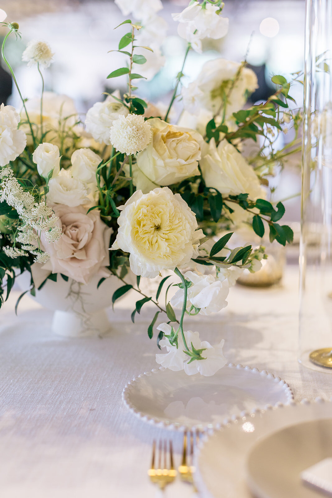 Low floral centerpieces for elegant wedding overflowing with white garden roses, ranunculus, butterfly ranunculus, scabiosa, lisianthus, sweet peas, and natural dark greenery. Floral hues of white, cream, and blush. Designed by Rosemary and Finch in