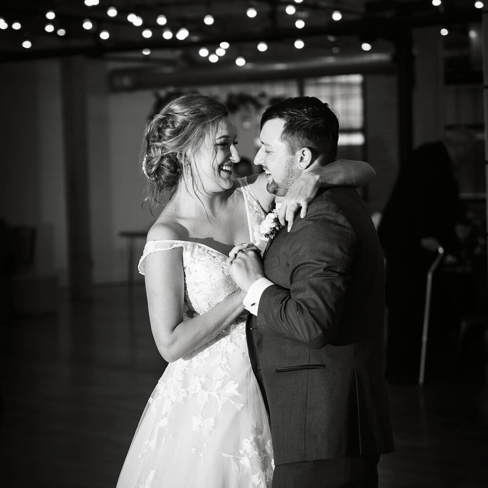 newlyweds dancing their first dance under lights in black and white