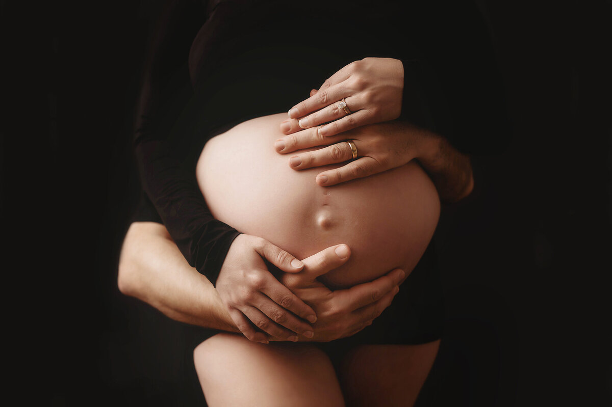 Expectant parents embrace pregnant woman's belly during Studio Maternity Photoshoot in Charleston, South Carolina.