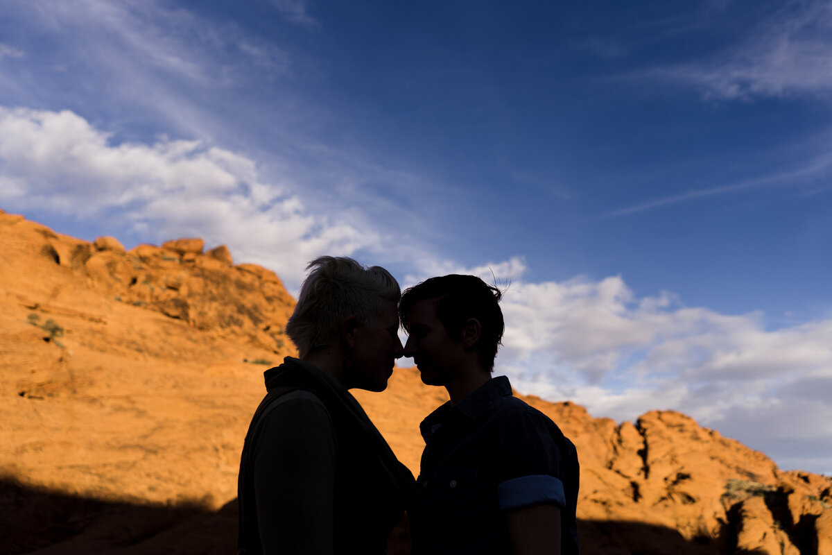 Two people about to kiss in the shadows with rocks behind them in the sun.