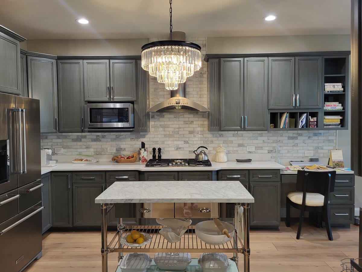 kitchen with marble rectangle white and green grey tones in it backsplash and creamy white with grey veining silestone countertops with grey green cabinets and island cart with marble top and stainless steel shelves with kitchen crockery