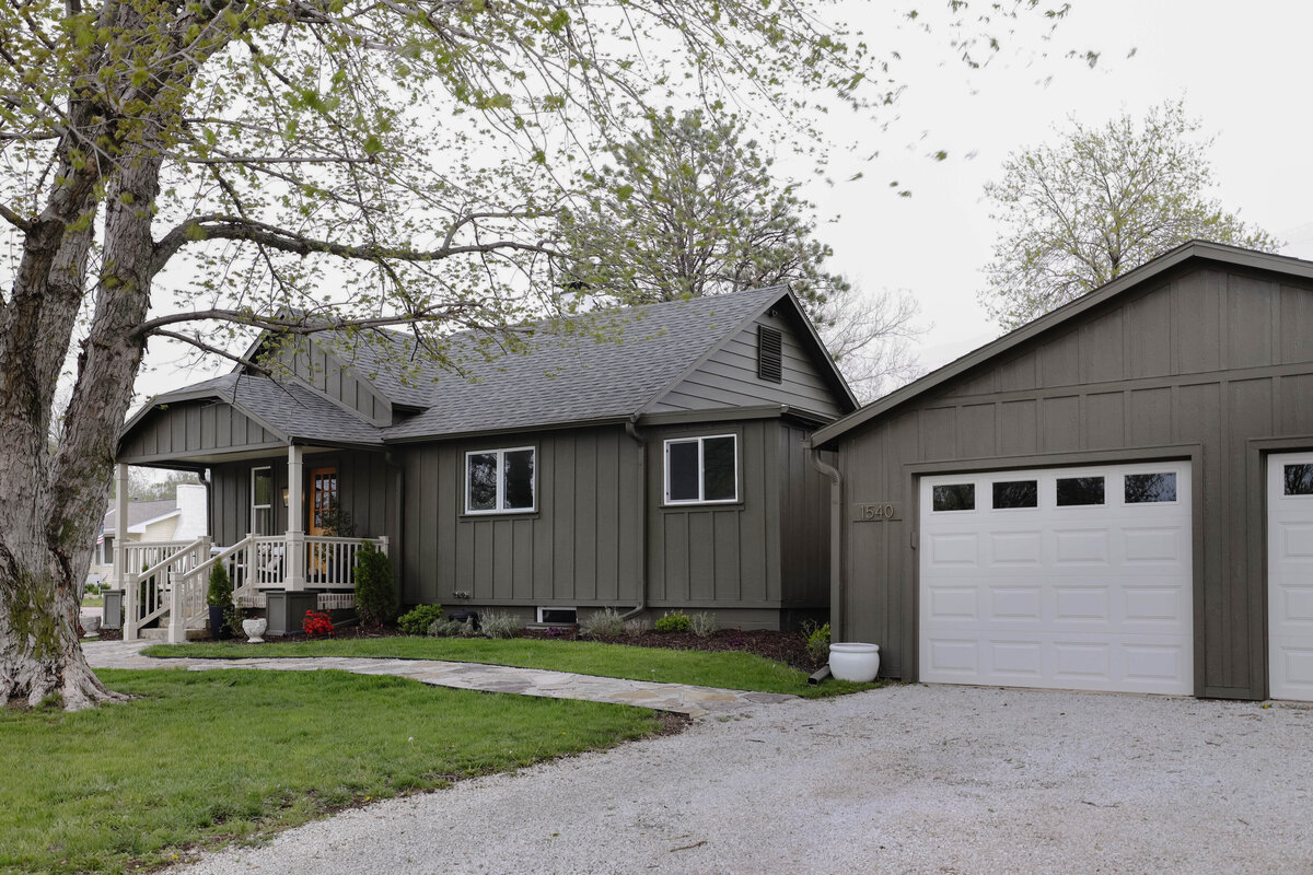 The exterior project by Nadine Stay. Board and batten siding install. Muddled Basil by Sherwin Williams exterior paint color. Flagstone path, brick front porch floor, and a custom built railing. Cabin exterior.