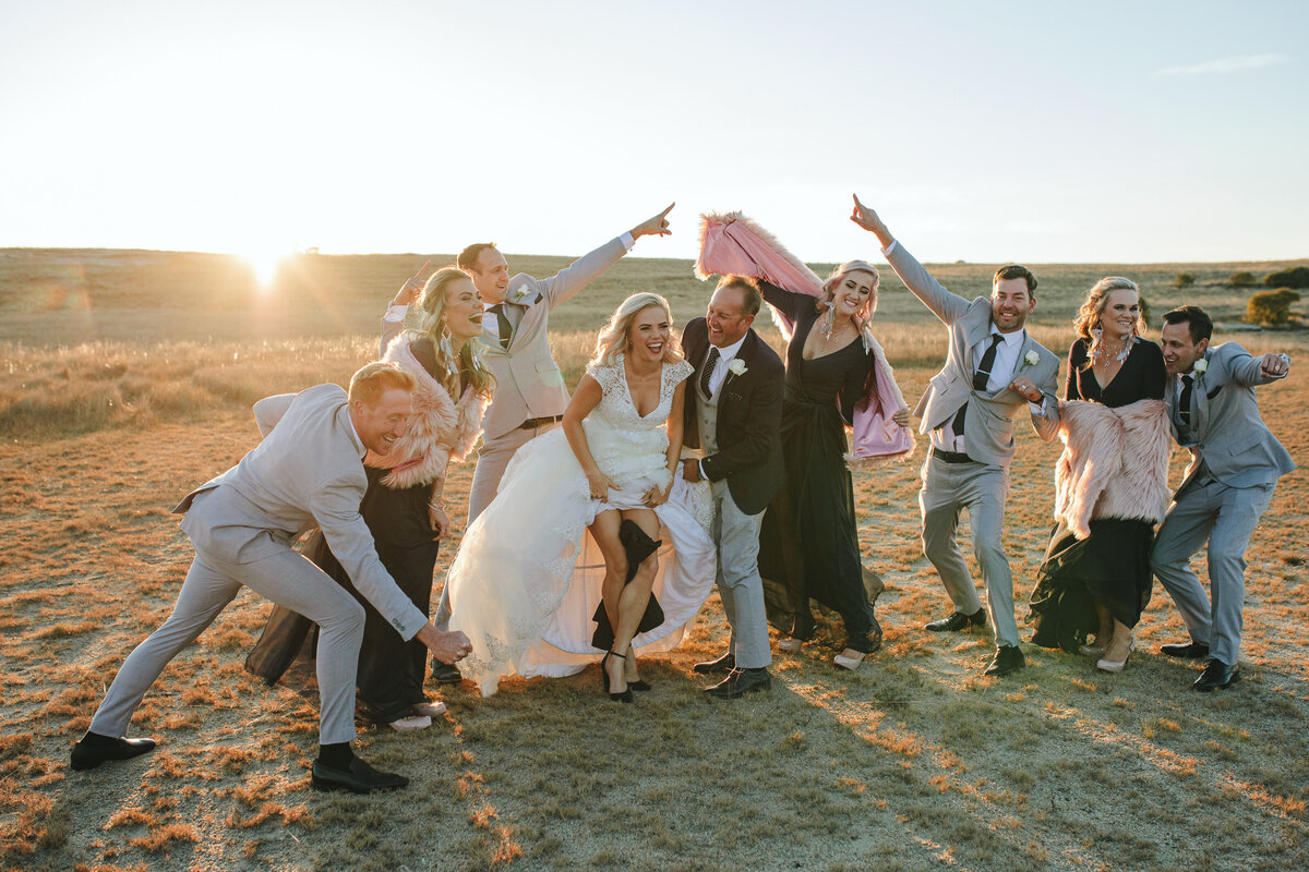 Bridal party laughing and having fun together as the sun sets behind them, captured in a spontaneous, documentary-style moment.