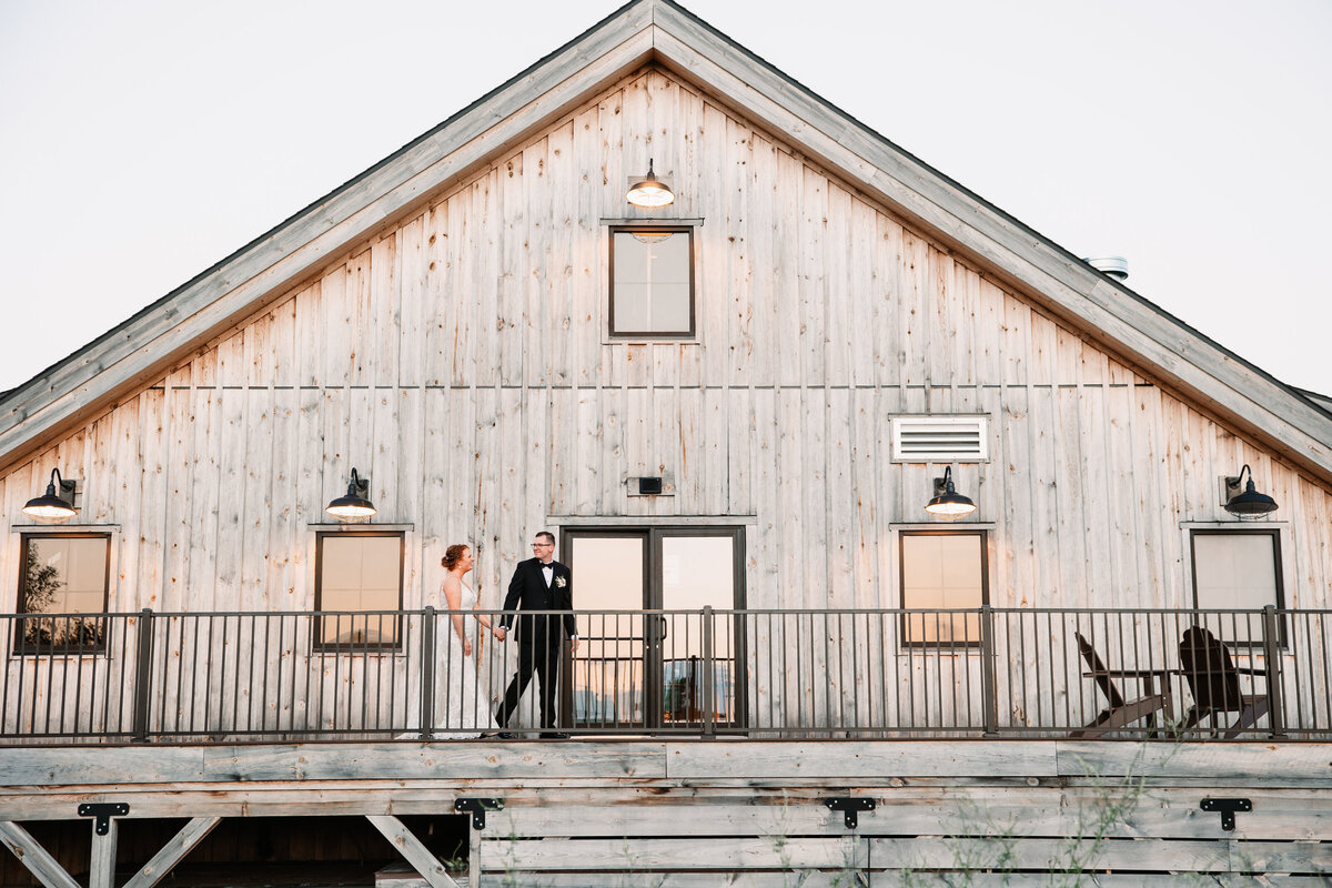 A bride and groom walk hand in hand on a patio of their venue at sunset