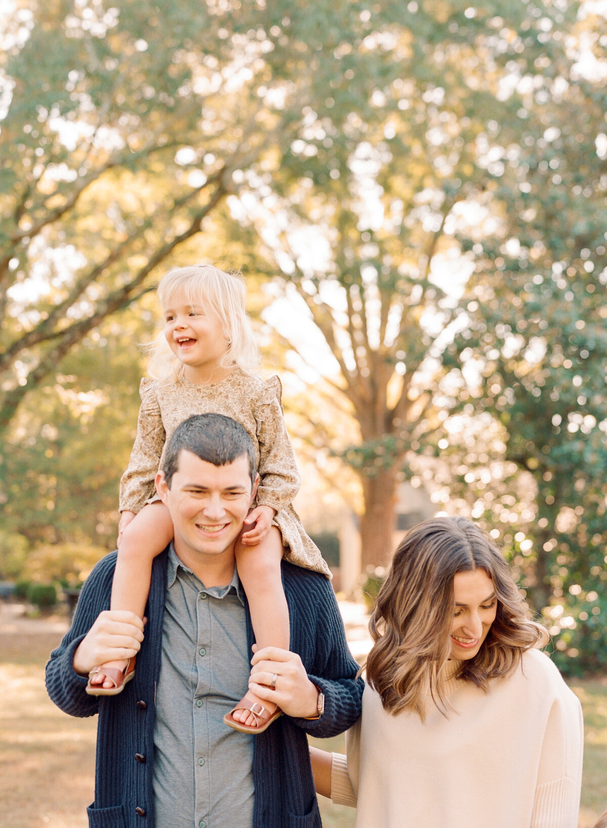 Daughter laughs as she sits on her dad's shoulders during a family session in Wake Forest NC. Image by Raleigh maternity photographer A.J. Dunlap Photography.