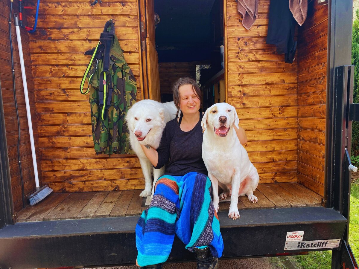 woman sitting with 2 white dogs on the back of a campervan