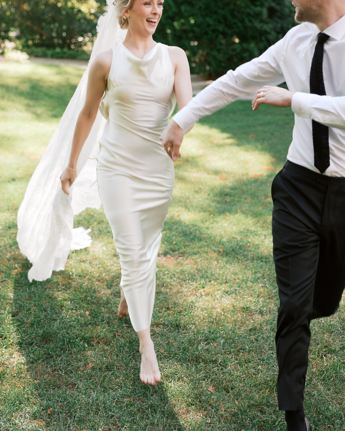 Bride barefoot and laughing while running hand-in-hand with groom, outdoor Dayton wedding captured by Philadelphia photographer.