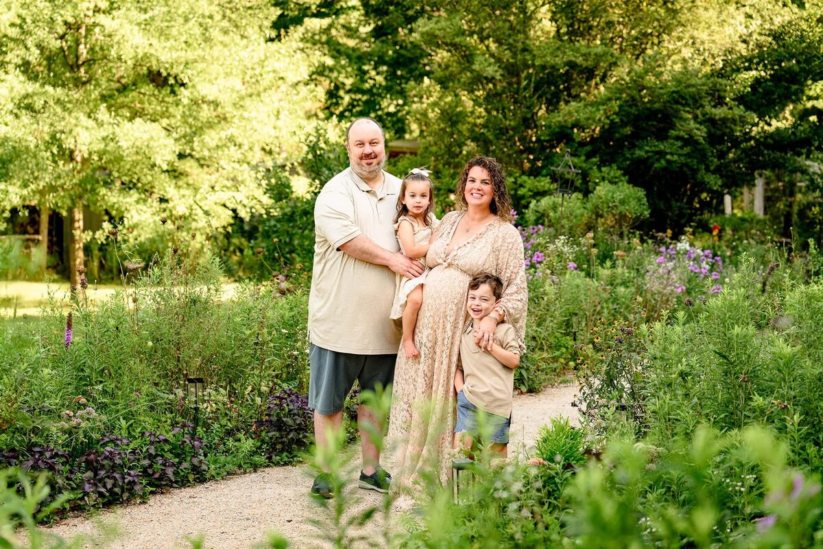 family of four standing in a flower garden for their maternity portraits all dressed in cream and natural tones