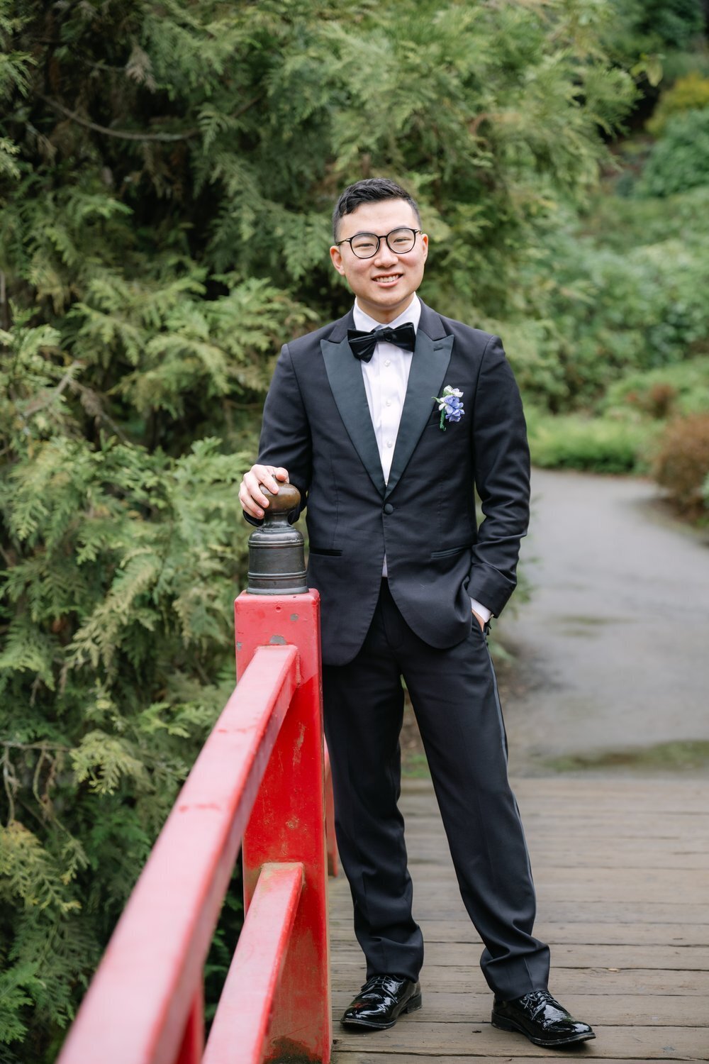groom posing at red bridge railing in kubota garden