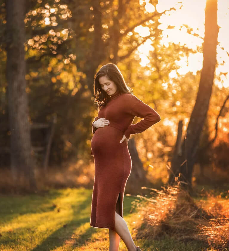 Pregnant mom holding belly with sun behind her