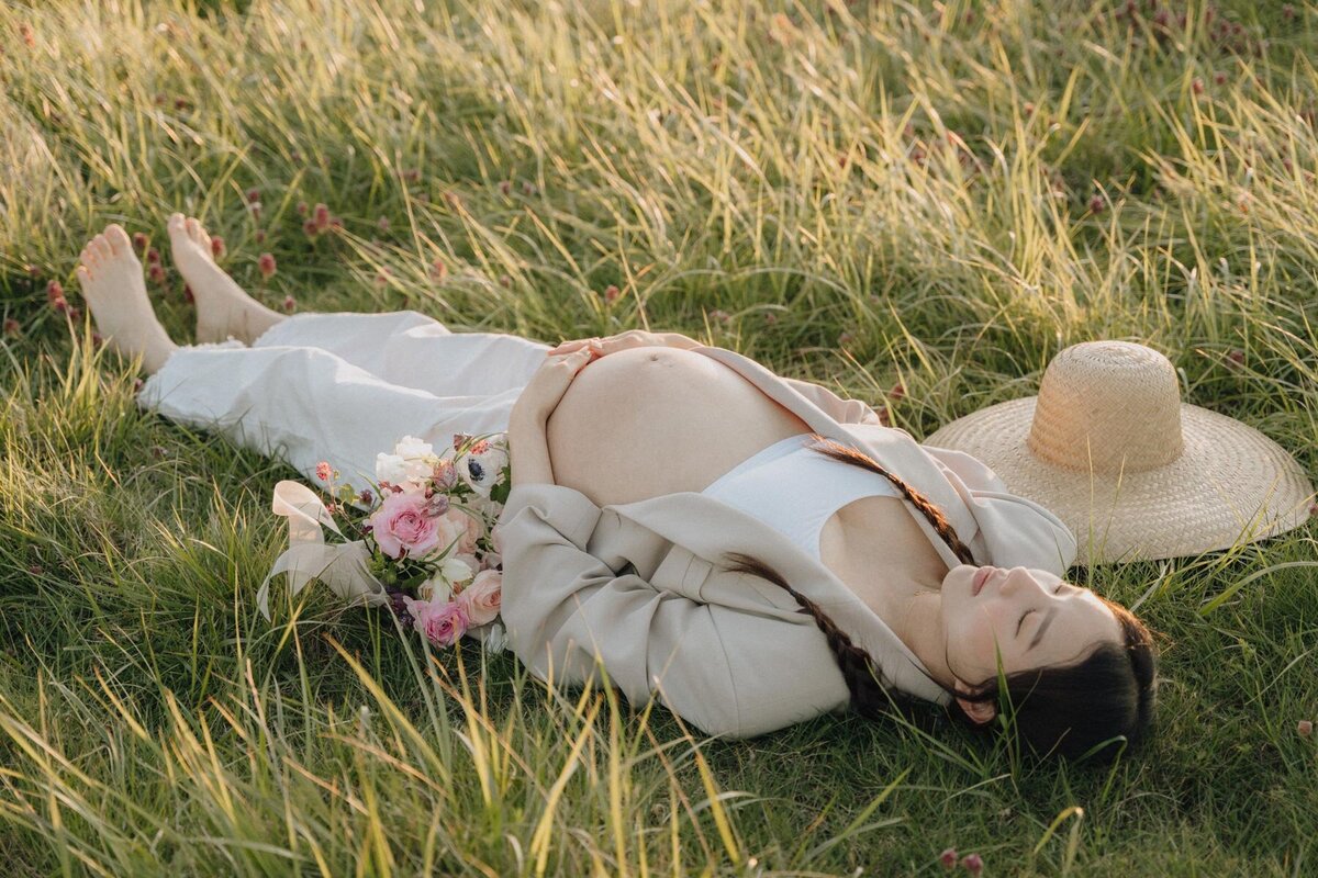 pregnant woman laying in the grass with sun shining on her