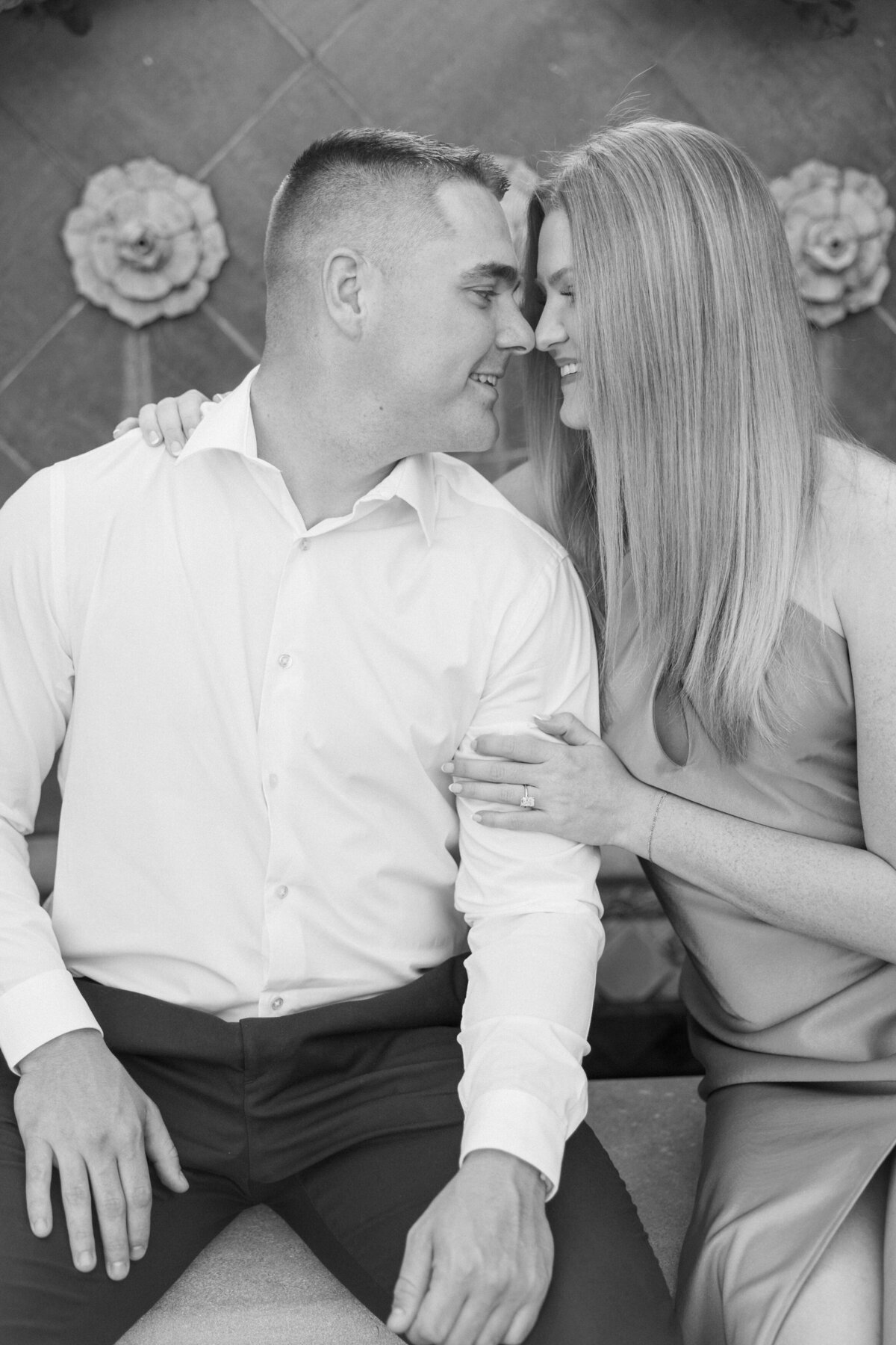 Black and white image of engaged couple touching noses sitting on Columbus park fountain shot by Philadelphia photographer.