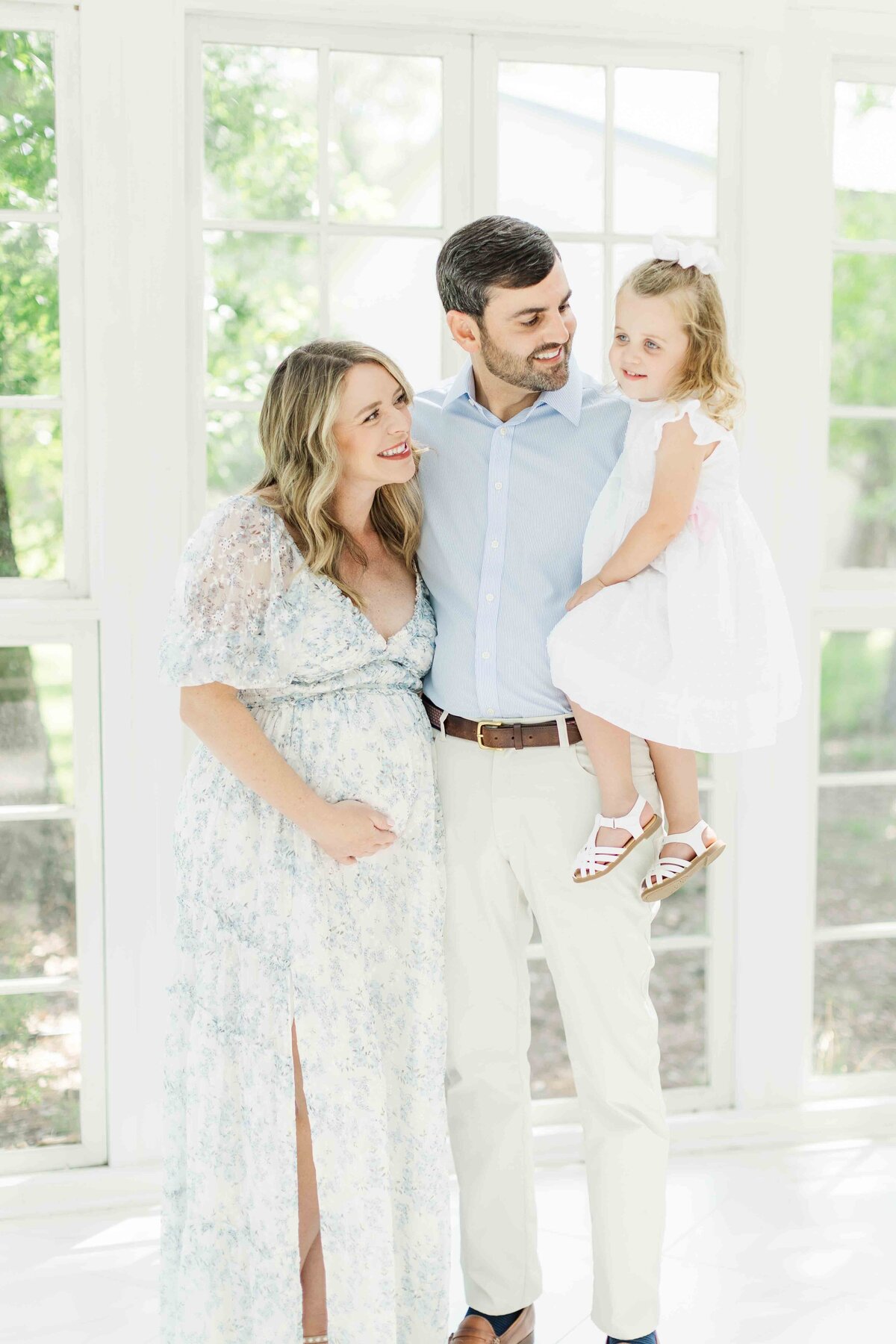 family of three smiles at each other for maternity photo session