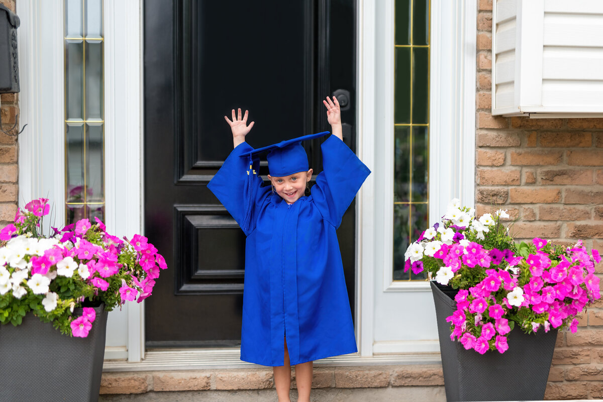 Kindergarten grad milestone photo of a girl beaming in her blue cap and gown—capturing the joy of her big achievement.