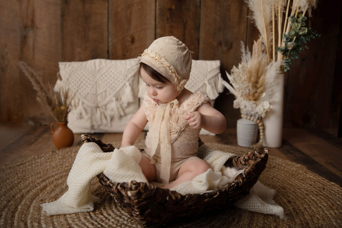 Baby girl wearing a vintage hat and onesie with a boho style sitting in a basket for her Burlington Kid photography session in Burlington, Ontario