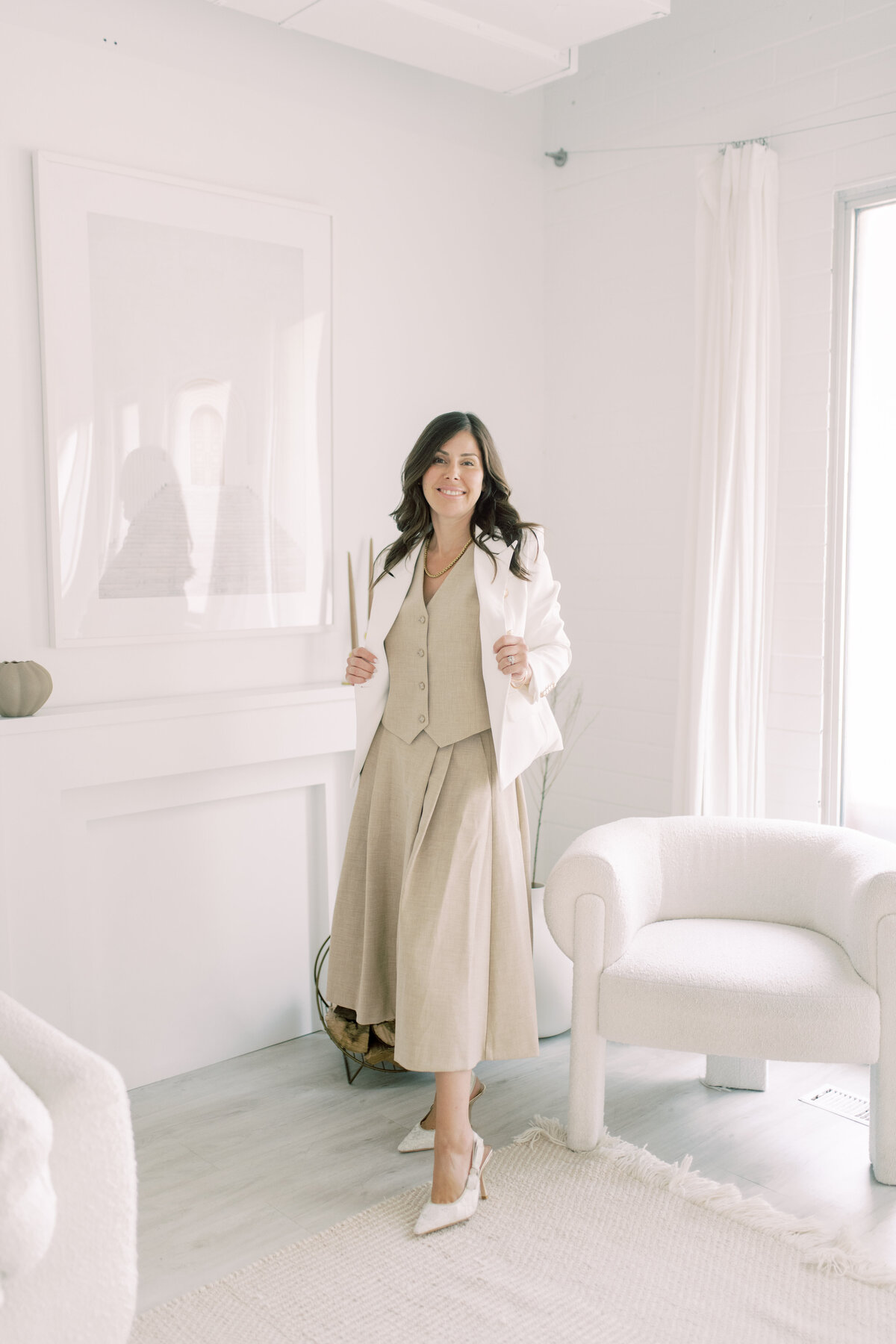 Close-up portrait of woman in linen skirt and white blazer, smiling in soft studio lighting
