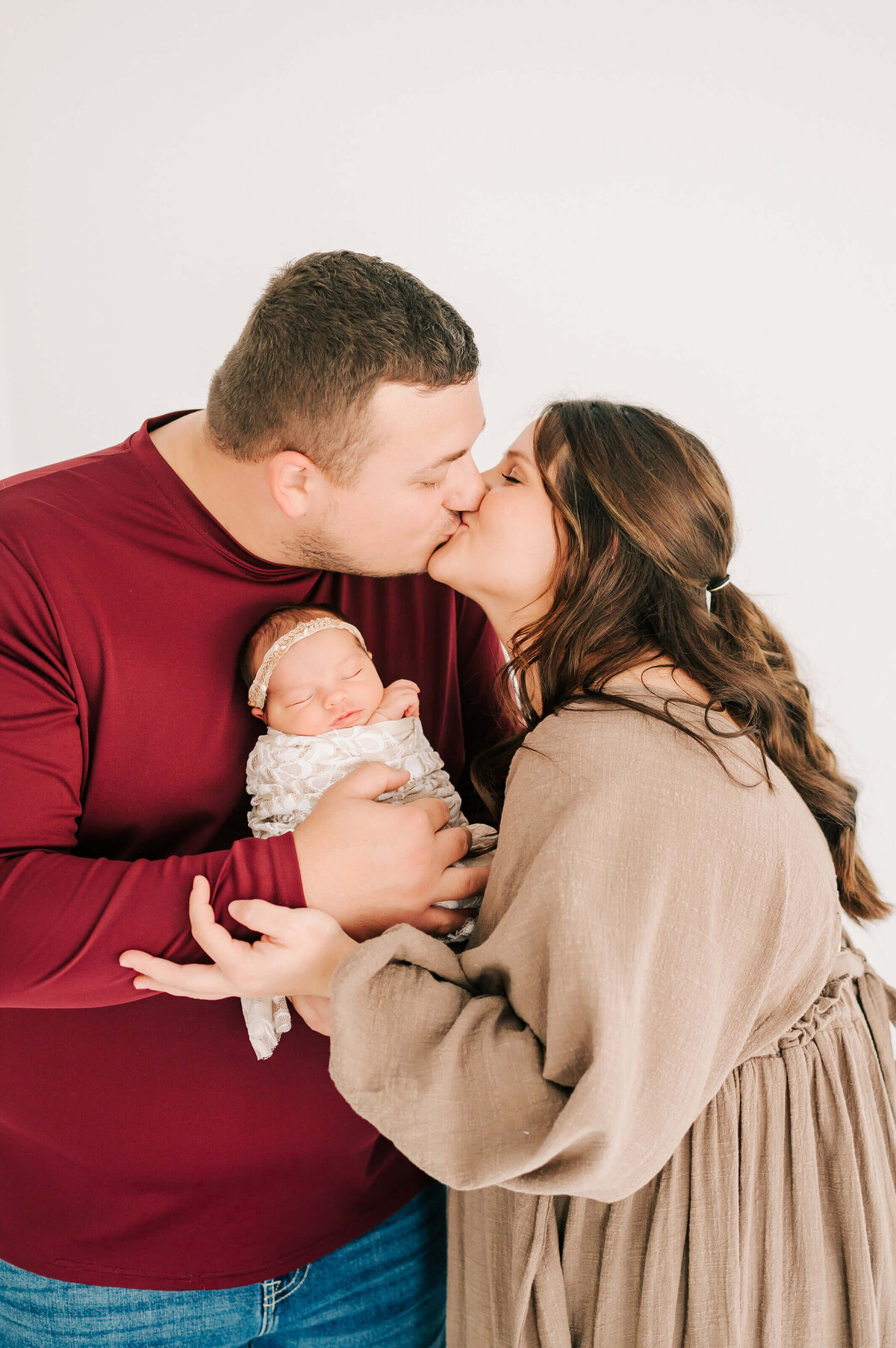 parents kissing holding baby girl in Springfield Mo newborn photography studio