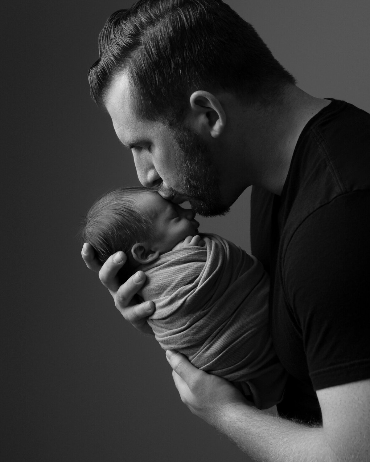 Black and white studio portrait of father kissing swaddled newborn in side profile pose | Georgetown newborn photographer