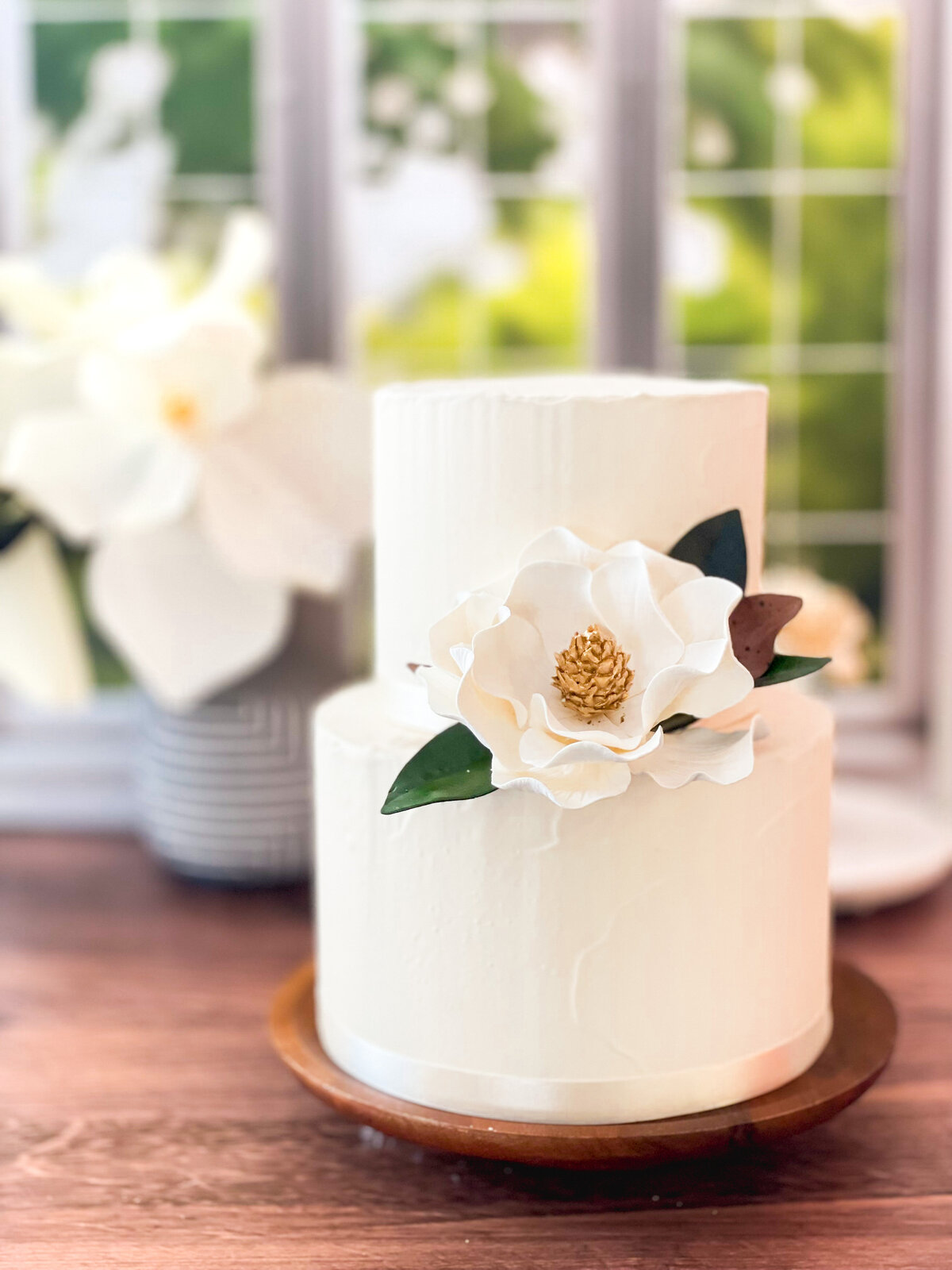 modern two tier cake with magnolia flower against a sunny window background