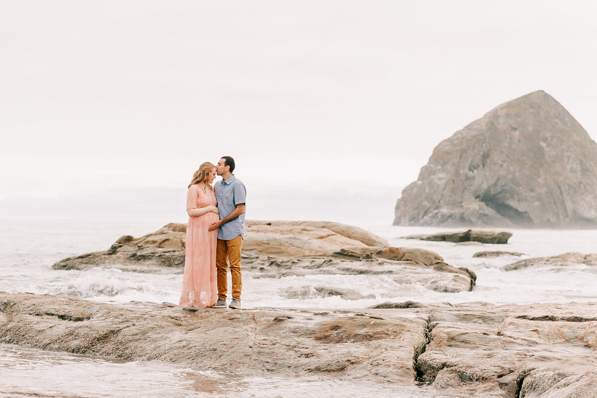 Beach fine art maternity photography in lincoln city oregon for portland family expecting a baby girl. He is kissing her on the head and they are  touching her belly