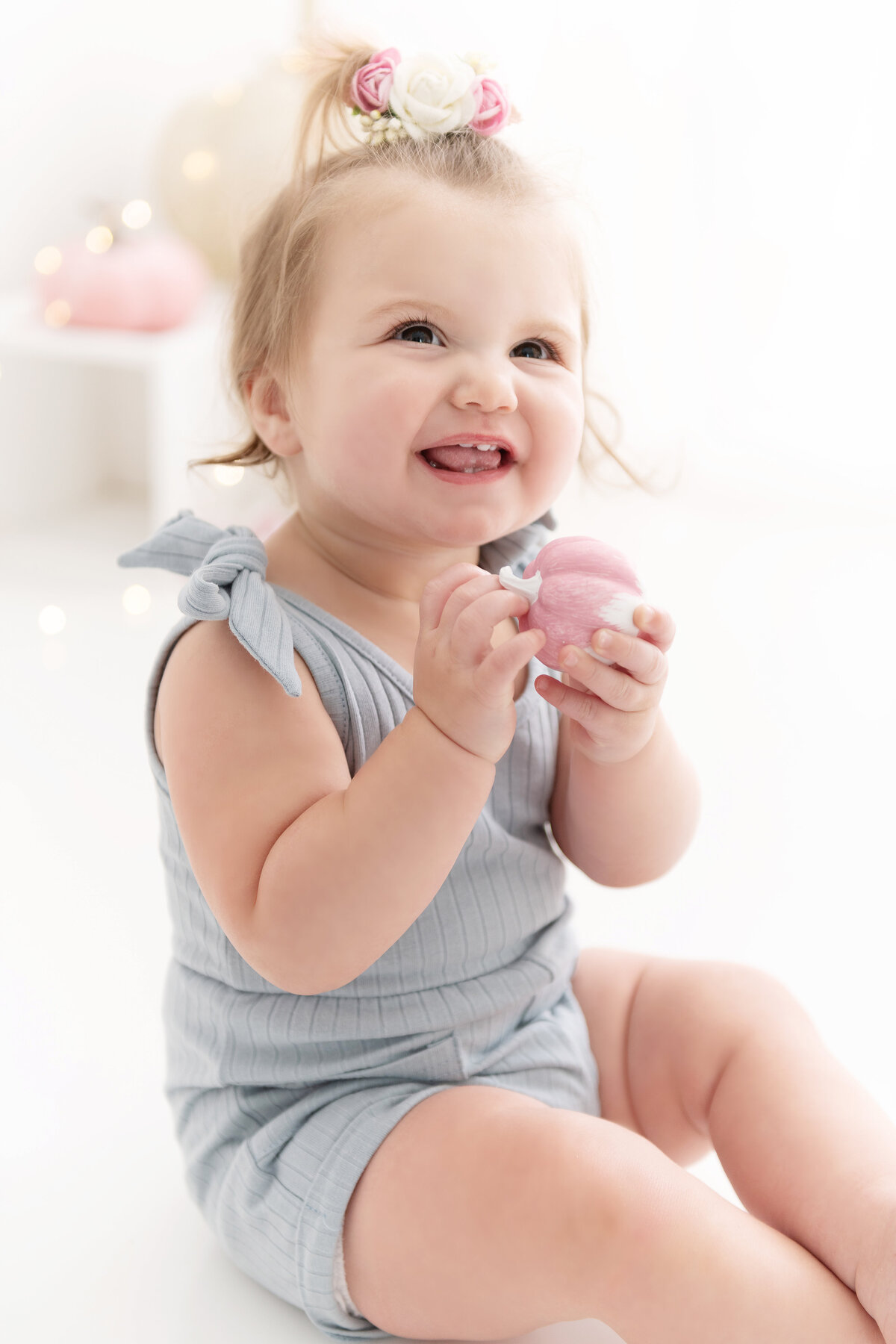 A toddler girl in a blue romper plays with a pink toy happily in a studio