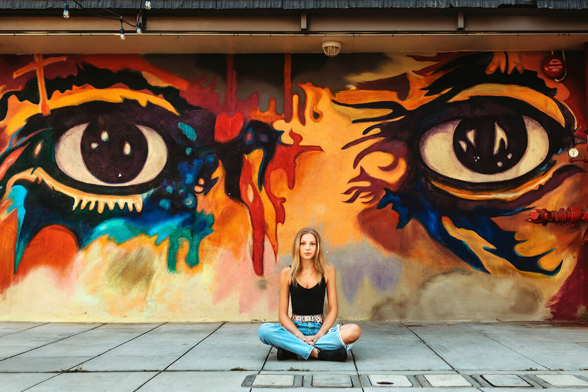 High school senior girl sitting in an alleyway with mural in downtown Fort Collins.