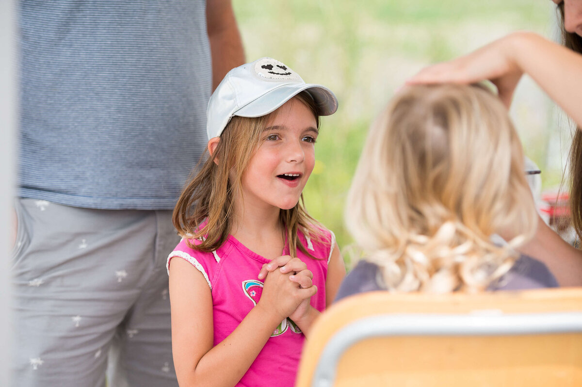 a little girl in a pink t-shirt showing excitement on her face while she waits to have her face painted during a corporate children's event.  Captured by Ottawa Event Photographer JEMMAN Photography COMMERCIAL