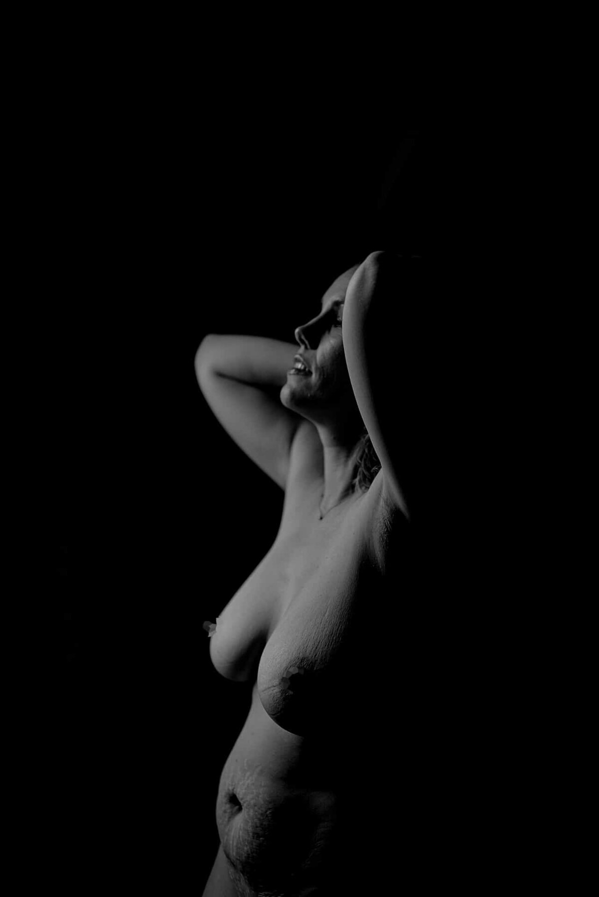 En naken kvinne med mammamage som står i lyset