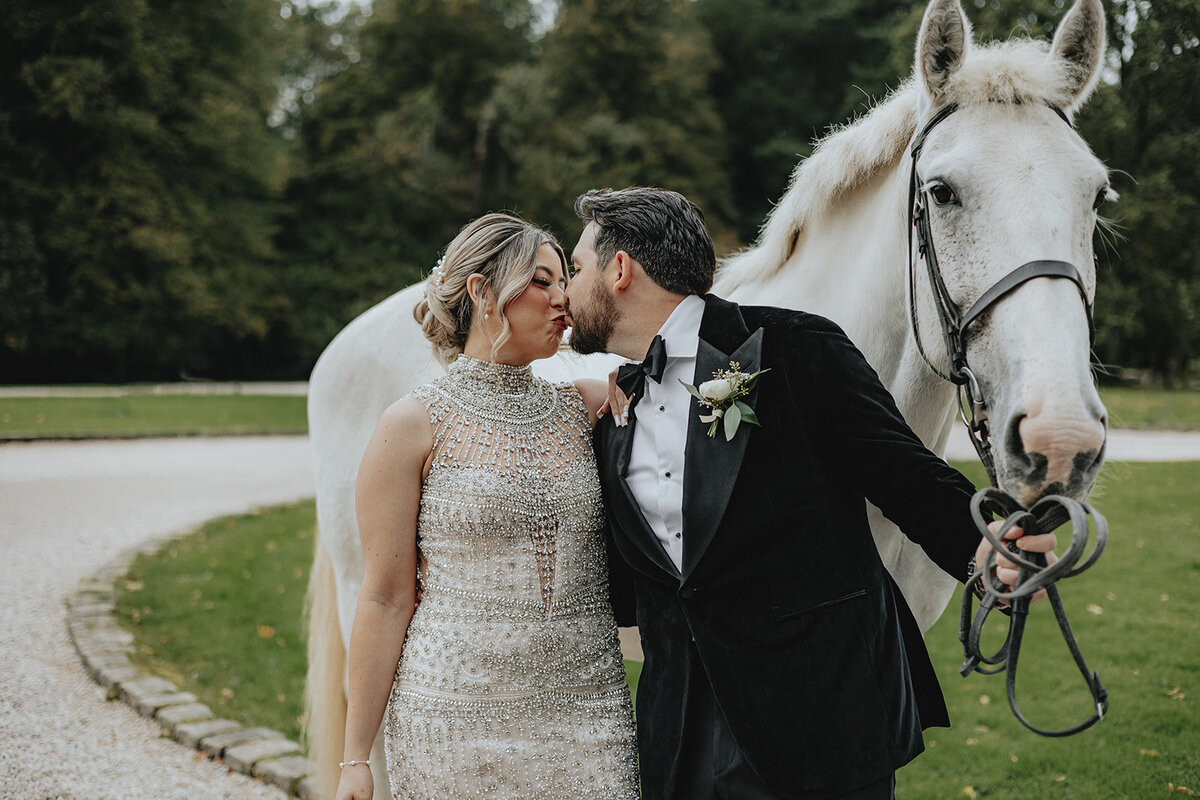 Bride and groom kissing next to white horse