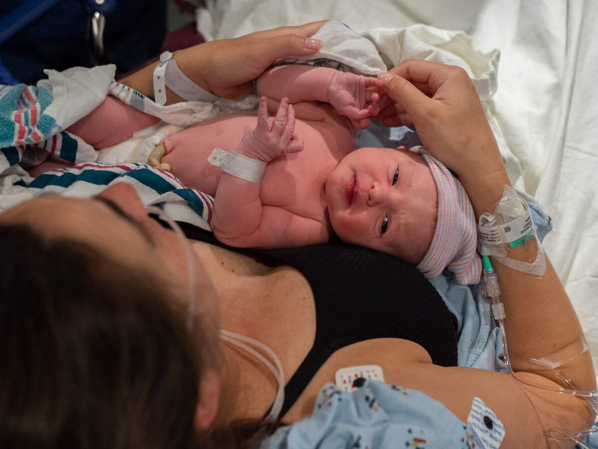a mother is holding a newborn baby while sitting in a hospital bed. the angle is from above looking down on the woman's head. Image captured by seattle birth photographer, Becky langseth.