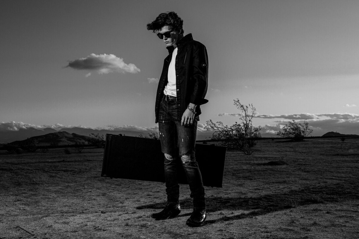 Musician portrait Richard Tichelman full length standing in desert holding guitar case black and white