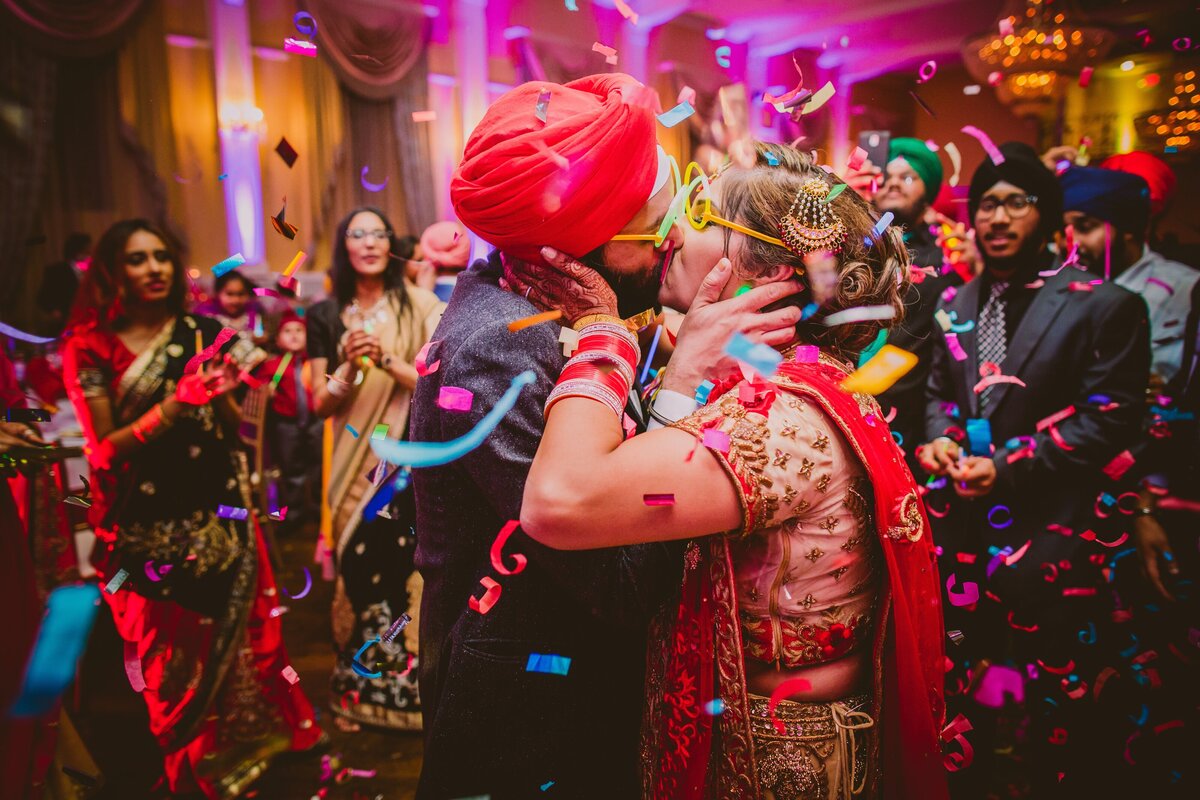 indian sikh wearing glow stick glasses couple share kiss at the wedding reception dance floor with confetti falling