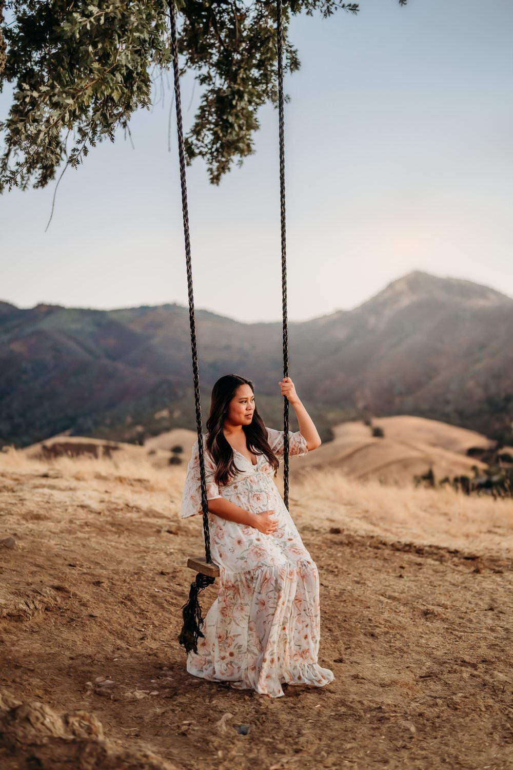 lafayette mama on a swing - she is pregnant and wears a floral maternity dress. she looks towards mt diablo