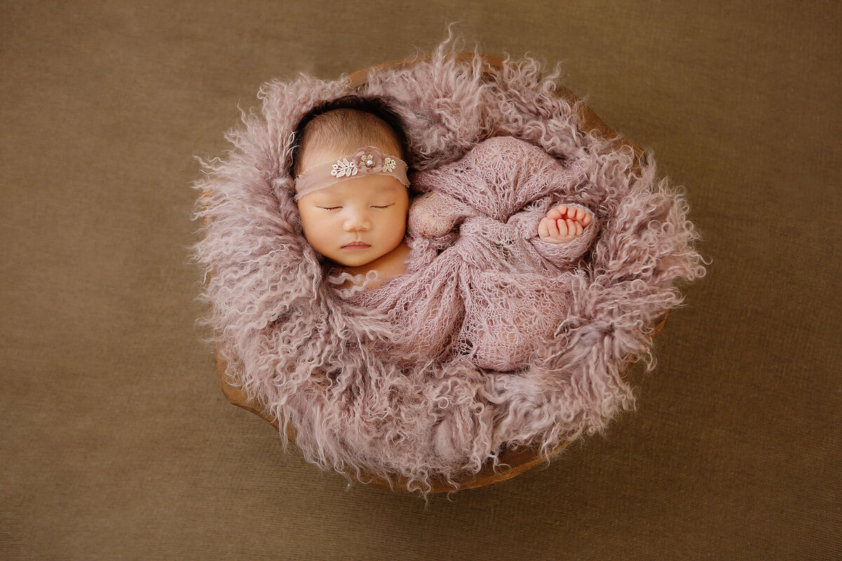 Newborn baby laying asleep wrapped in a swaddle in a bowl at newborn session