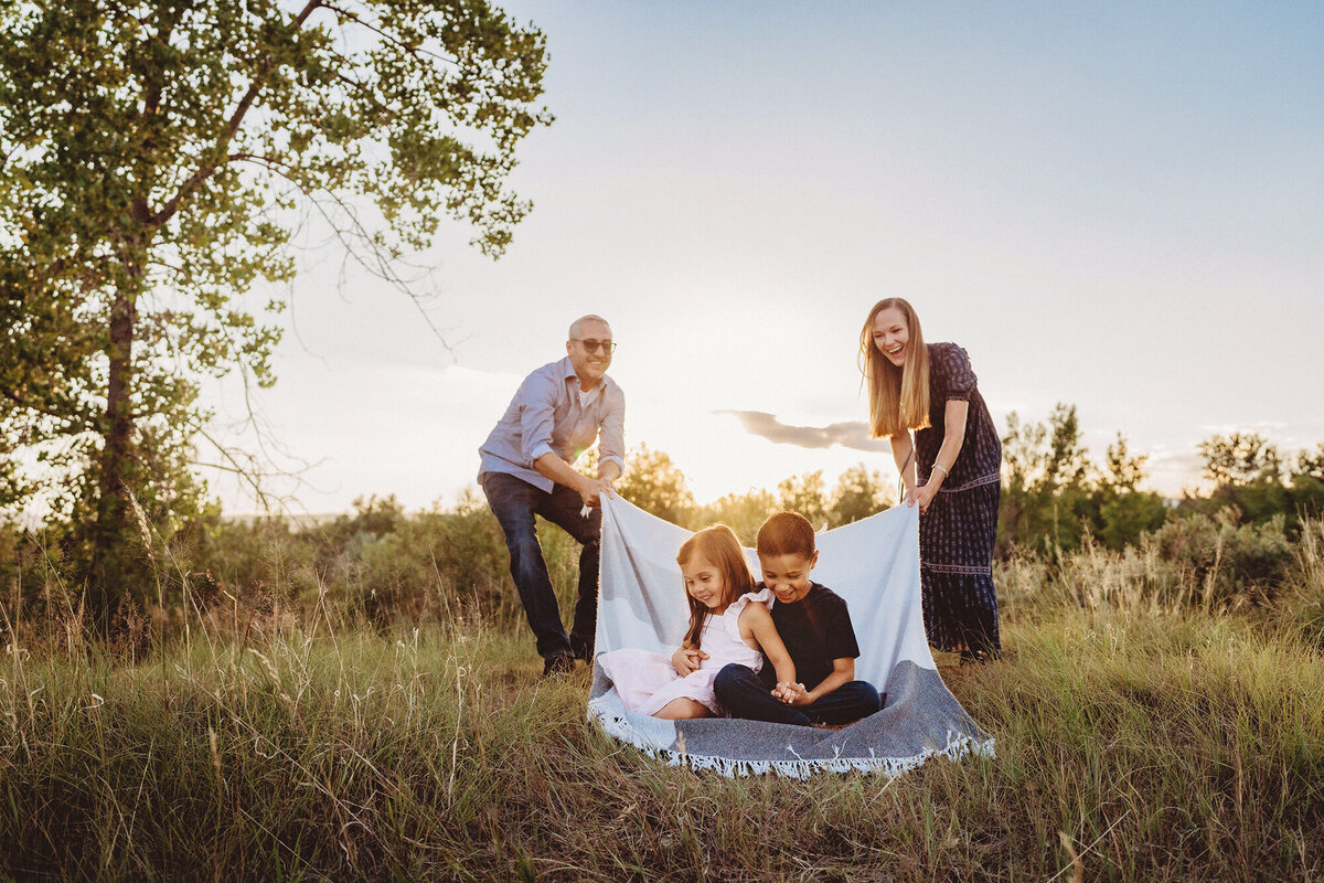 Parents have fun pulling thier two young children on a blanket during a summer family photoshoot in Lakewood, Colorado.